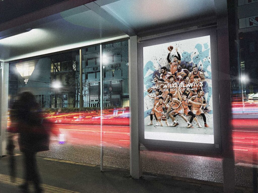 夜のバス停に掲出されたバスケットボールチームのポスター。街の光跡とともにチームの熱量が伝わる印象的なシーン
